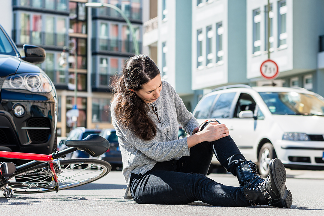 Full length of an injured young woman experiencing severe pain caused by knee sprain or fracture after bicycle accident in the city