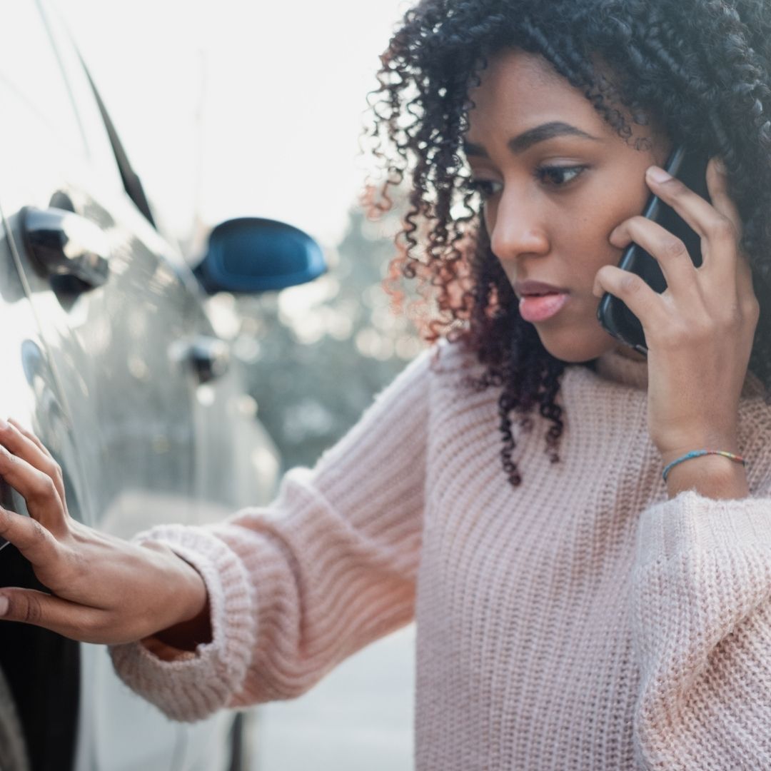 A woman looking at the damage on her car after an accident.