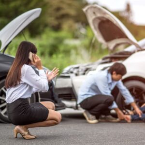 people outside after a car accident. a woman is kneeling on a cell phone while looking at a male help an injured female