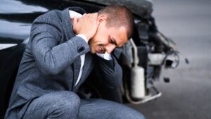 persona con una expresión de dolor sentada cerca de un auto destrozado