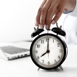 a person placing their hand on a clock in front of a laptop