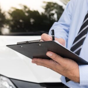 persona escribiendo en un portapapeles frente a un auto