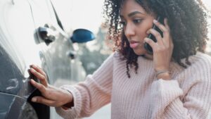 Woman on the phone examining the damage to her car