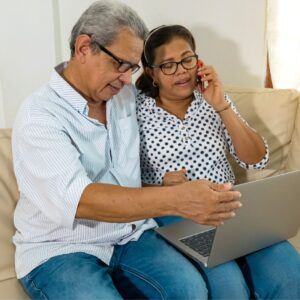 dos personas que usan una computadora portátil mientras una hace una llamada telefónica