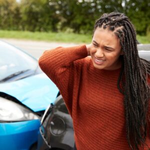 Woman at the scene of an accident holding her neck and grimacing. 