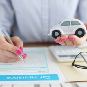 Woman holding a toy car in her hand while filling out an insurance form. 