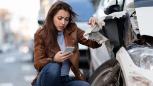Woman kneeling and looking distressed while inspecting a car after an accident.