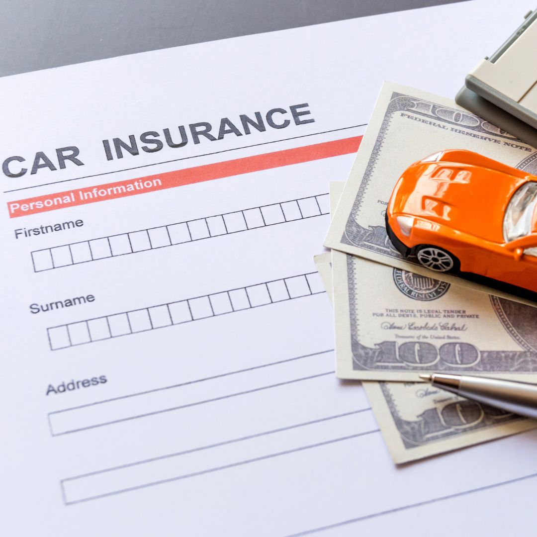 Piece of paper with "Car Insurance" written at the top and a toy car stacked on top of multiple $100 bills. 