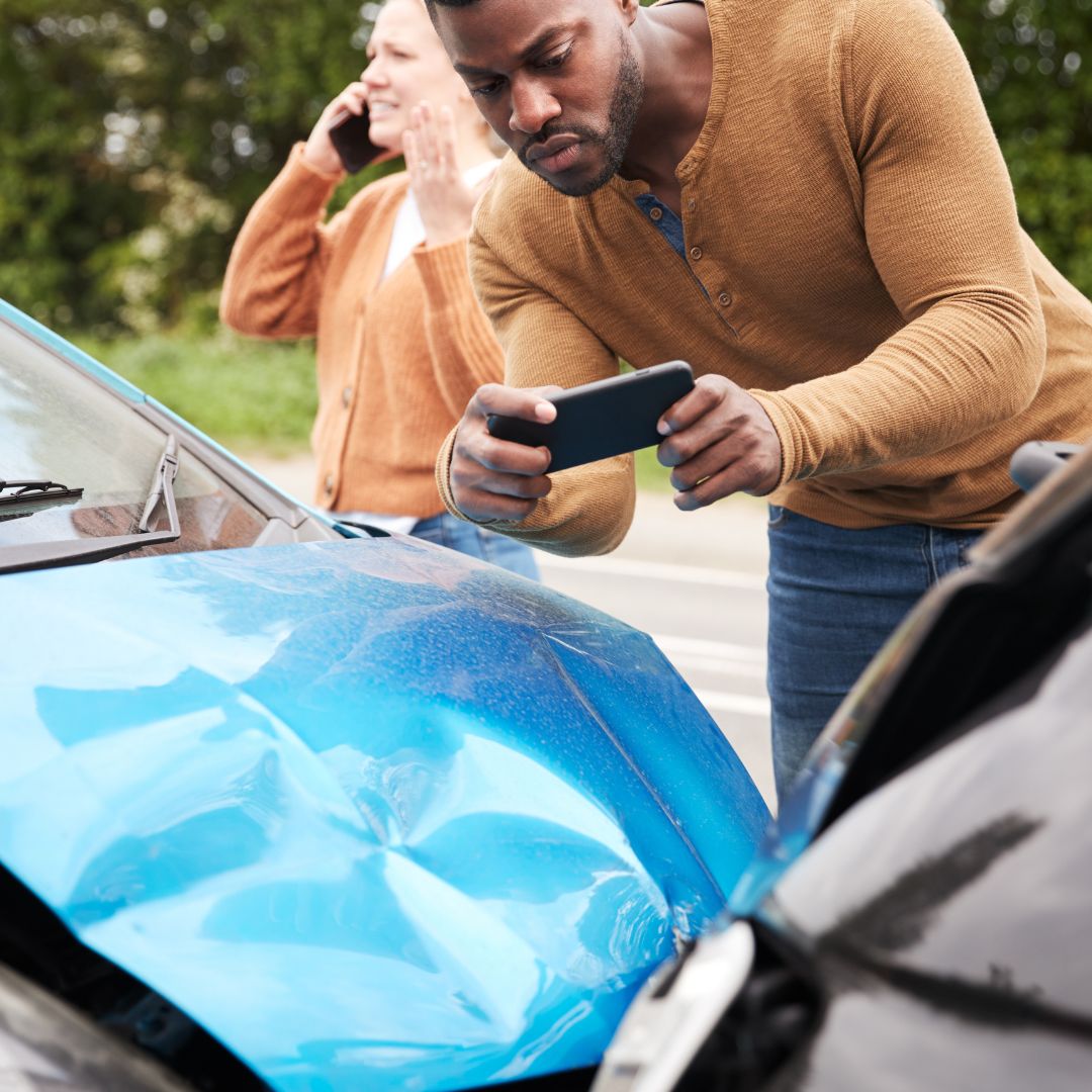 man taking pictures of a car accident with a woman on the phone in the background. 