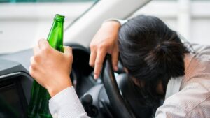 Person sleeping on steering wheel while drinking a beer
