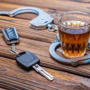 A glass of whiskey next to handcuffs and car keys