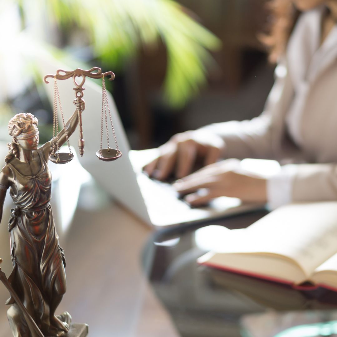 Lawyer in her office. Statue of Justice with scales and lawyer working on a laptop.