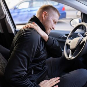 Man sitting in his car grabbing his shoulder in pain