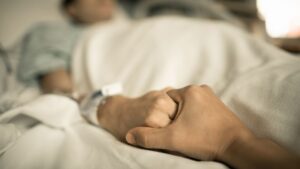 Una persona dándole la mano a otra en una cama de hospital