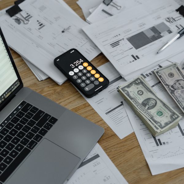 Un portátil junto a una calculadora y documentos