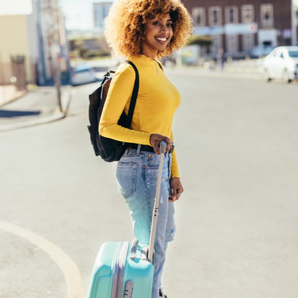 A woman carrying luggage crossing the street