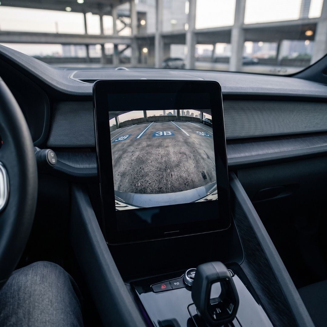 Car dashboard backup camera display showing a real-time rear view in a parking garage.