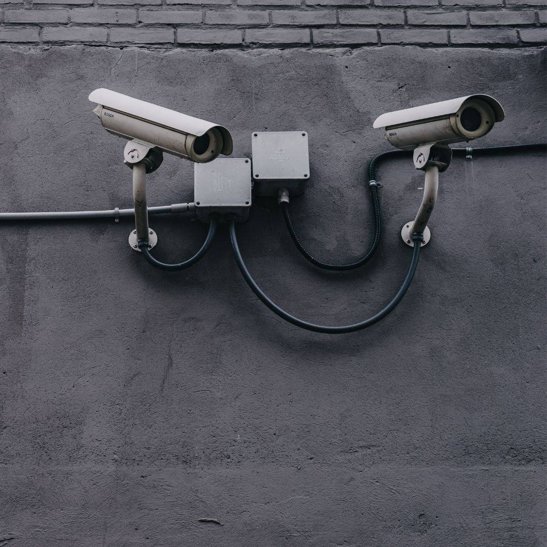 Surveillance security cameras mounted on a wall above a parking lot.