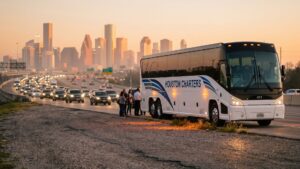 Modern commercial charter bus stopped on a Houston interstate highway shoulder with hazard lights.