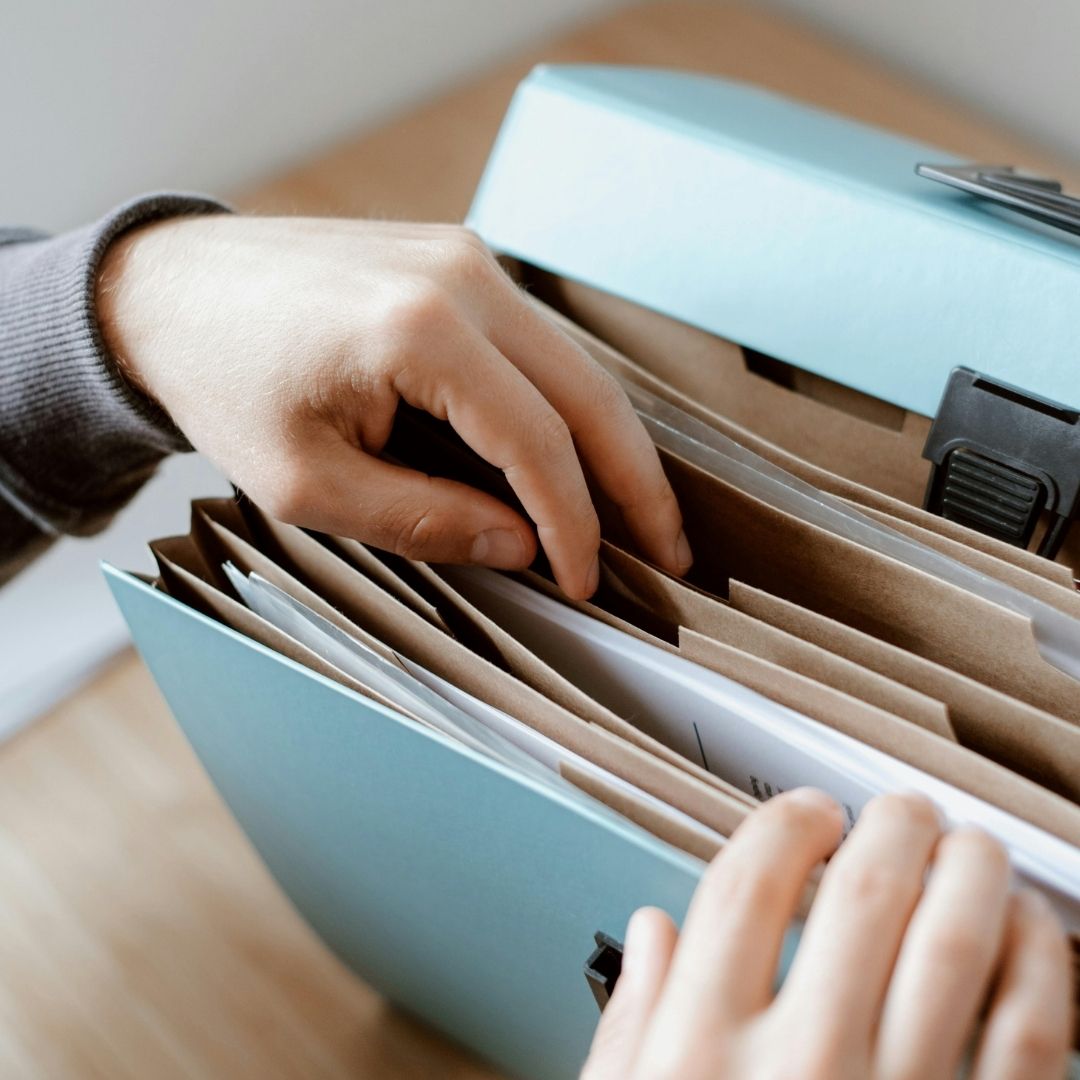 Hand searching through legal documents and records in a file box.