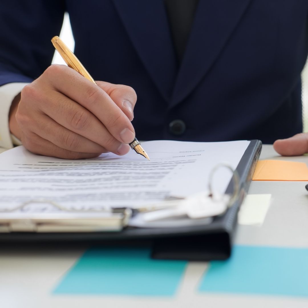 Person in a suit signing legal insurance documents with a fountain pen.