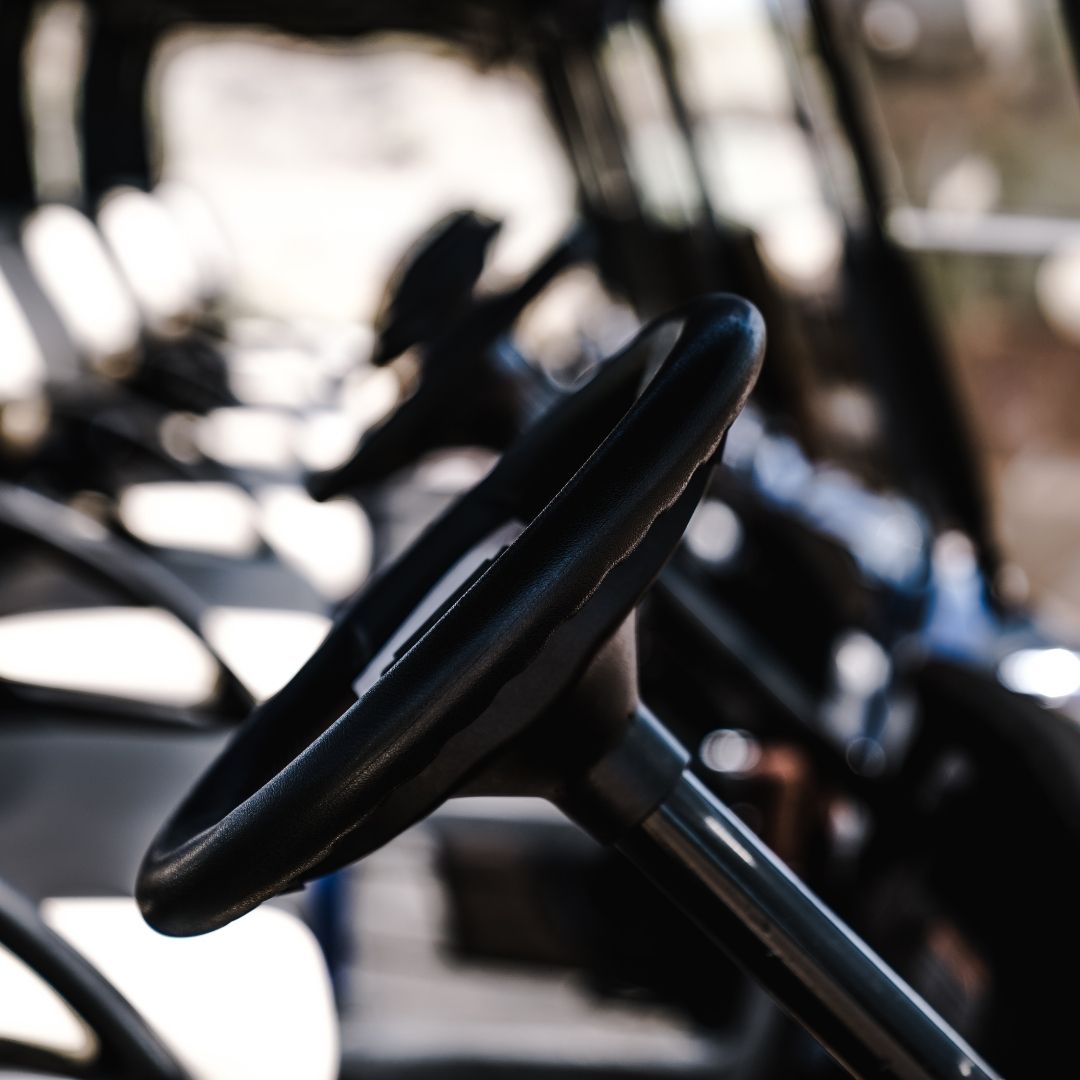 Close-up of a golf cart steering wheel in a row of parked carts.