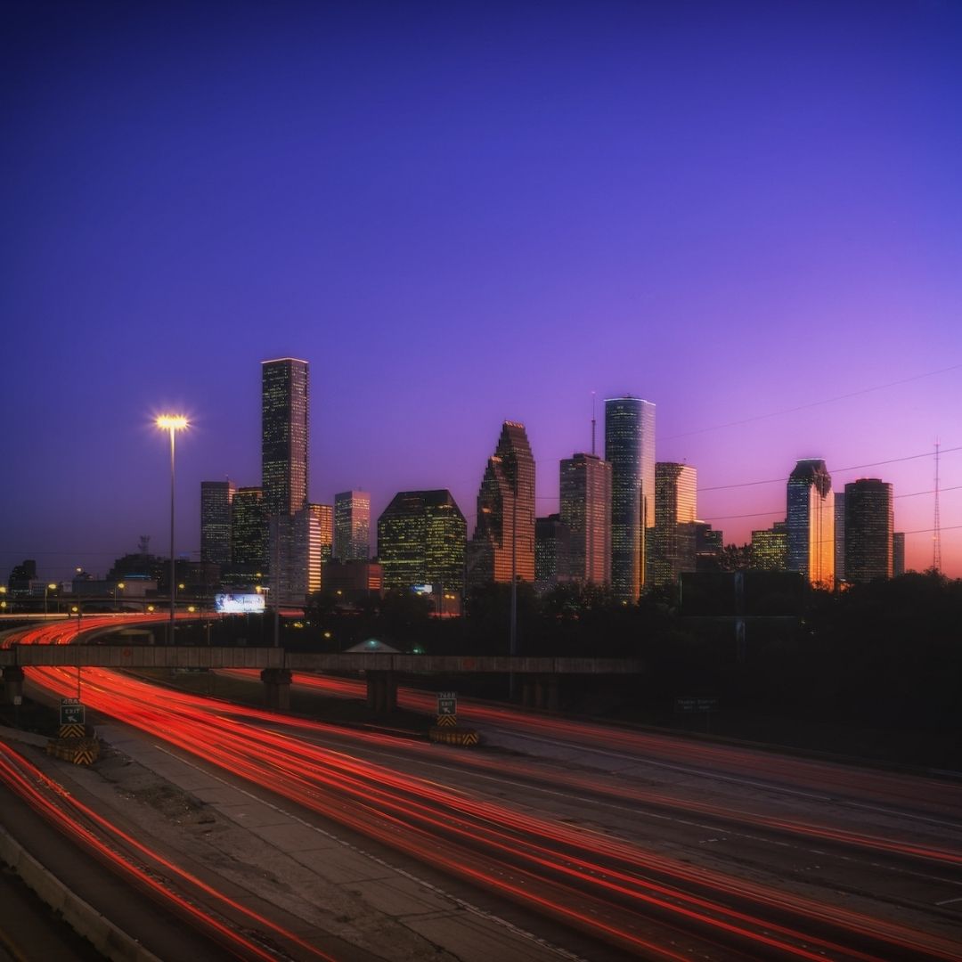 Houston skyline at dusk with long-exposure red car light trails on the freeway.